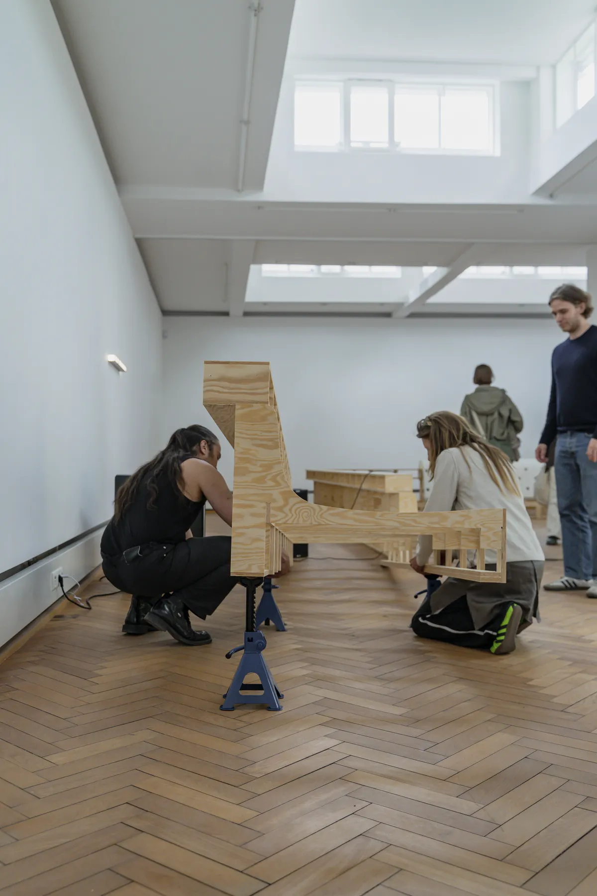Wide gallery view showing the complete wooden framework installation with natural light from skylights illuminating the minimalist white space at Trust Trust, Lübeck, 2025.